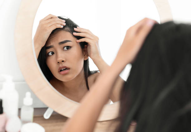 Woman examining hair loss near the scalp in the mirror