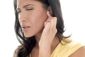 Person experiencing ringing noise in ear, holding side of head in discomfort