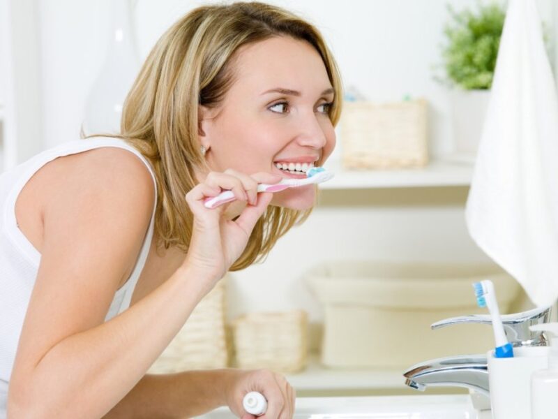 • Person brushing teeth with a timer beside the sink to indicate proper brushing duration