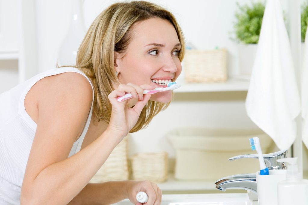 • Person brushing teeth with a timer beside the sink to indicate proper brushing duration
